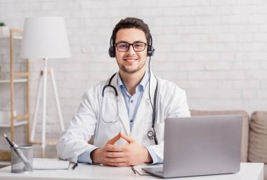 Sağlık blogu. Kulaklıklı genç doktor laptopuyla masada oturuyor.