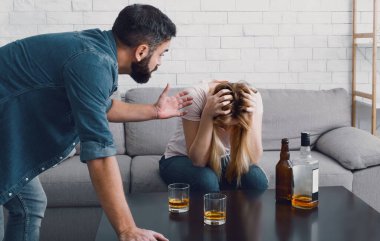 Sarhoş skandalı. Kadın başını tutup kanepeye oturuyor, kızgın adam karısıyla küfrediyor.