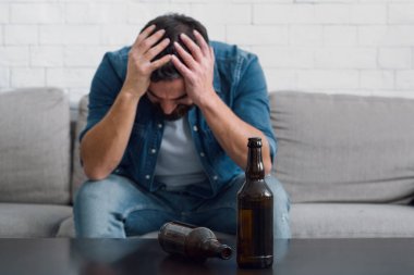 Üzgün adam başını tutup kanepeye oturur, boş şişeleri masaya koyar, kapat.