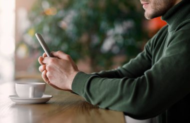 Kafede oturan, çay içen, akıllı telefon kullanan bir adam.