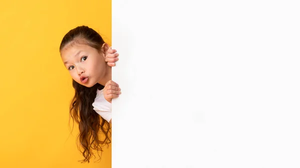 Ásia menina escondendo atrás branco publicidade cartaz — Fotografia de Stock