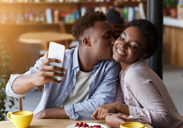 Afroamerykanin robi selfie całując swoją dziewczynę w miejskiej kawiarni — Zdjęcie stockowe