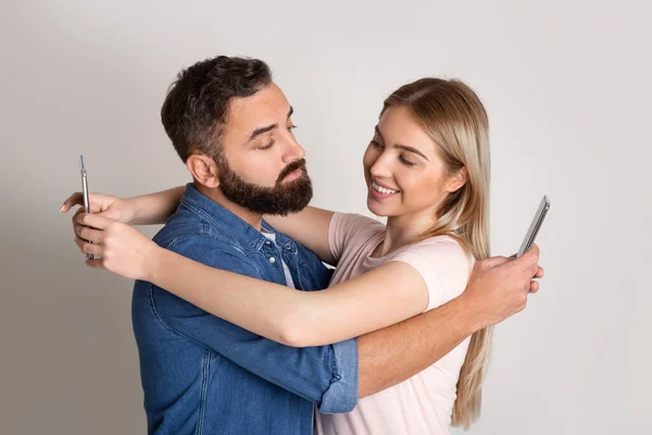 Sosyal ağlara ve ihanete bağımlılık. Erkek ve kız sarılıyorlar ve akıllı telefonlara bakıyorlar. — Stok fotoğraf