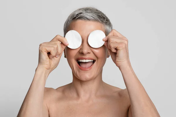 Skincare Fun. Positive Mature Woman Covering Eyes With Cotton Pads And Laughing — Stock Photo, Image