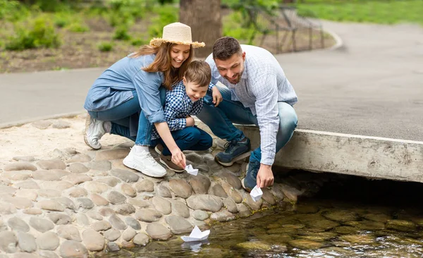 공원에 있는 작은 강에서 종 이 보트를 가지고 노는 사랑 스러운 아이와 그 의 부모 — 스톡 사진