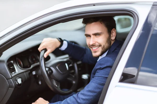 Bello imprenditore sorridente seduto sul sedile del conducente della sua auto in città — Foto Stock