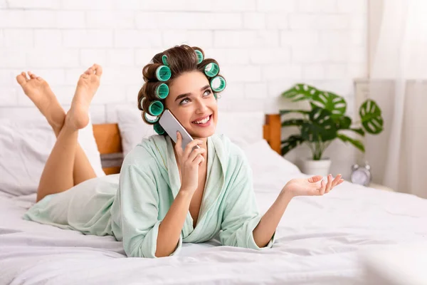 Glad hemmafru pratar på mobiltelefon ligger på sängen inomhus — Stockfoto