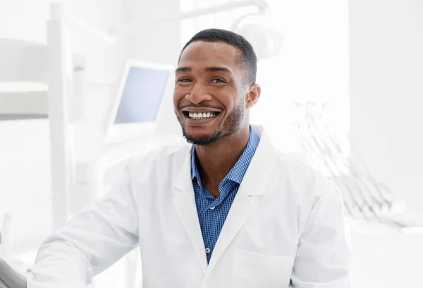 Bonito dentista preto sorrindo sobre o moderno fundo clínica odontológica — Fotografia de Stock