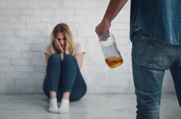 Hombre amenaza a mujer con botella en la mano, llorando mujer está sentado en el suelo — Foto de Stock