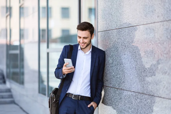Empreendedor confiante verificando mensagens em seu telefone celular perto da parede do edifício do escritório na cidade — Fotografia de Stock