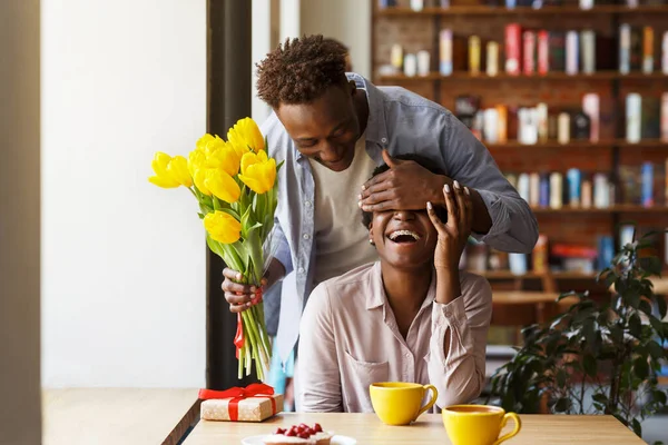 African American guy giving flowers to his girlfriend in urban cafe — Stock Photo, Image