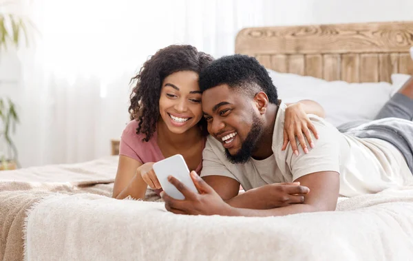 Gelukkig zwart paar met behulp van smartphone op bed — Stockfoto