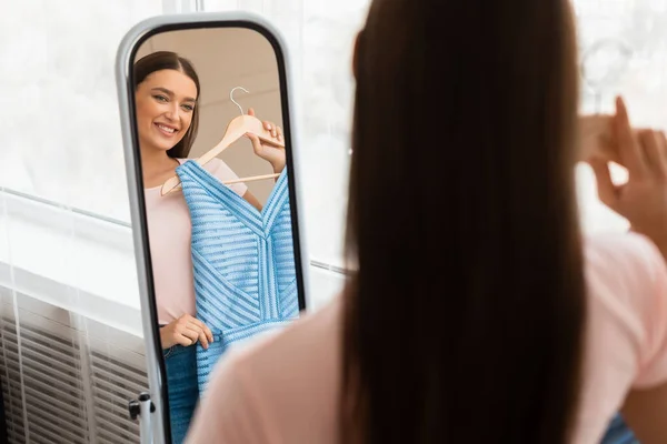 Dívka drží nové šaty při pohledu na zrcadlo stojící doma — Stock fotografie