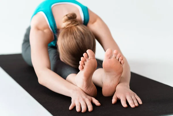 Mujer milenaria inclinándose hacia adelante en la estera de yoga, fondo blanco — Foto de Stock