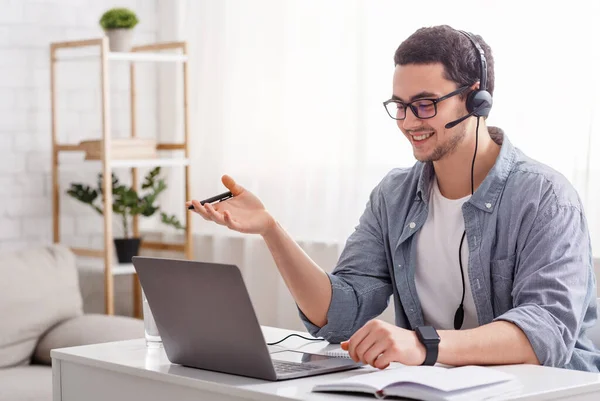 Profesor en línea y trabajo desde casa. Tipo en gafas y auriculares hablando con el estudiante —  Fotos de Stock