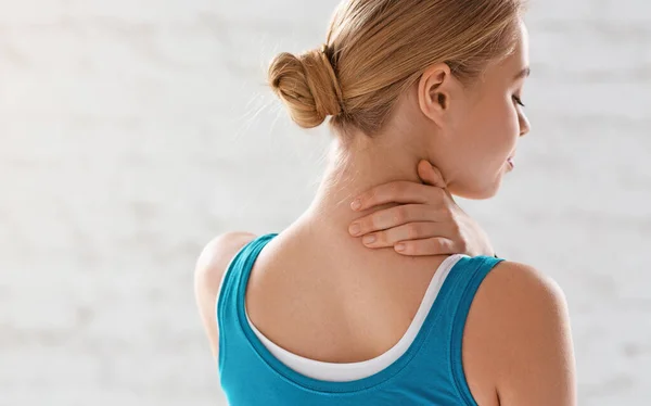 Lesiones deportivas. Chica atlética sintiendo dolor en el cuello contra el fondo blanco, espacio de copia —  Fotos de Stock
