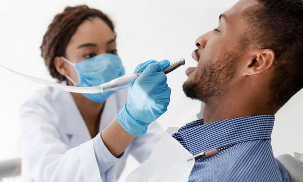 African woman dentist drilling patient teeth, close up