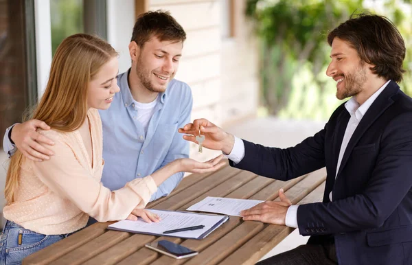 Joyful jovem família recebendo a chave para sua nova casa de agente imobiliário, ao ar livre — Fotografia de Stock