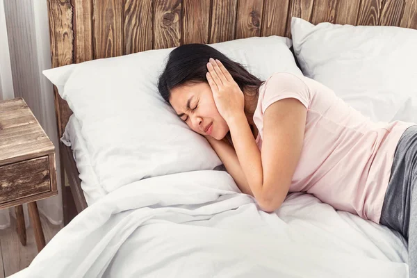 China chica cubriendo aguijón orejas tener otitis acostado en cama —  Fotos de Stock