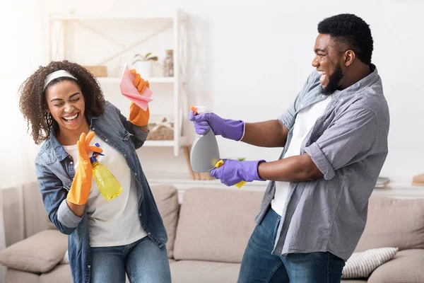 Alegre casal afro-americano brincando com pulverizadores enquanto limpam apartamento juntos — Fotografia de Stock