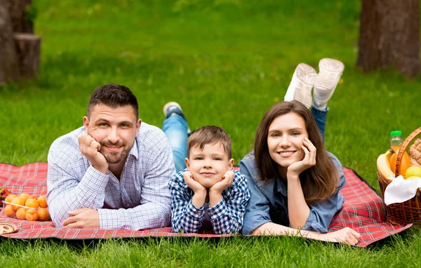 Divertidos momentos familiares. Adorable niño con los padres acostados en la manta durante el picnic en el parque — Foto de Stock