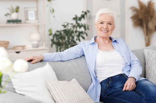 Sonriente anciana posando en el sofá en la sala de estar en casa —  Fotos de Stock