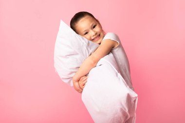 Komik küçük kız pembe arka planda yastığa sarılıyor.