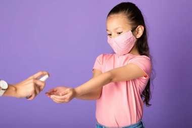 Stüdyo duvarında izole edilmiş dezenfektan kullanan maskeli bir kız.