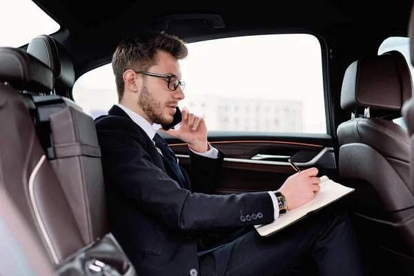 Empresário escrevendo em notebook em carro de luxo — Fotografia de Stock