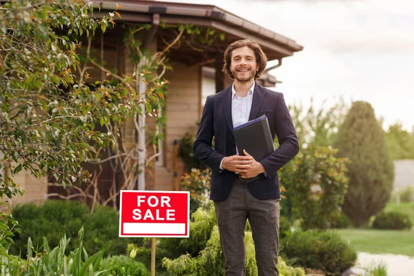 Feliz agente de bienes raíces de pie frente a la nueva casa en venta, al aire libre. Espacio en blanco —  Fotos de Stock