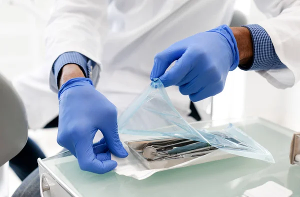 Mãos de dentista preto abrindo conjunto selado de ferramentas odontológicas — Fotografia de Stock