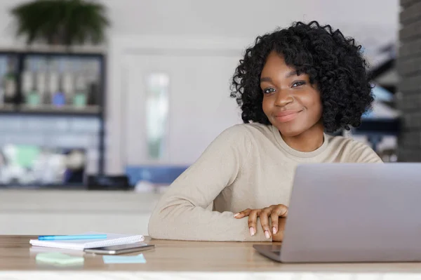 一个漂亮的非洲女孩一边在咖啡店边摆姿势一边用笔记本电脑 — 图库照片