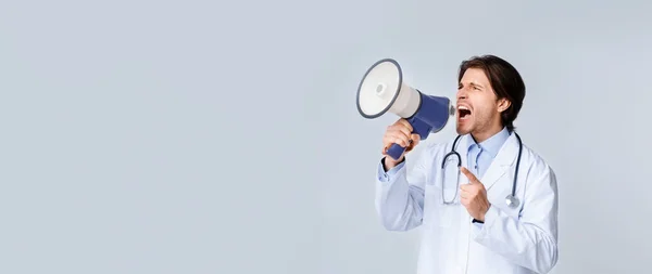 Angry male doctor shouting with megaphone at copy space on light background
