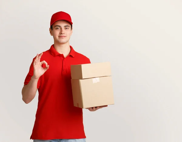 Hervorragende Arbeit. Zusteller hält Pakete in der Hand und zeigt Schild perfekt mit der Hand — Stockfoto