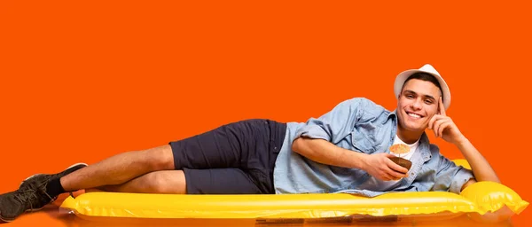 Szczęśliwy turysta leżący na żółtym gumowym materacu, delektujący się koktajlem — Zdjęcie stockowe