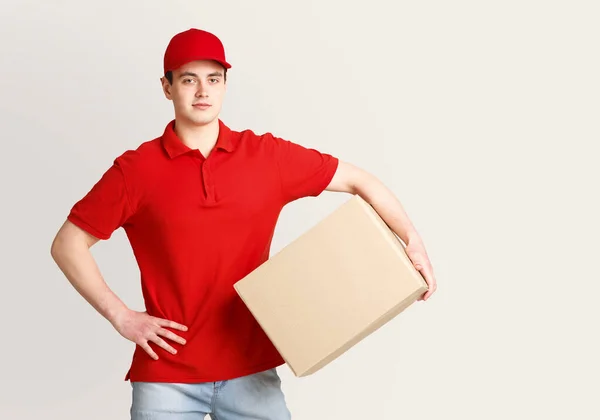 Entrega a domicilio moderna. Mensajero en uniforme rojo sostiene el paquete debajo de su brazo y espera al cliente — Foto de Stock