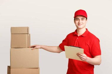 Postacı tarafından paket kontrolü. Üniformalı gülümseyen kurye not almak için tableti tutuyor ve elini karton kutunun üzerine koyuyor.