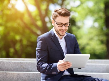 Başarılı iş lideri, güneşli bir günde yeşil parkta tablet kullanıyor.