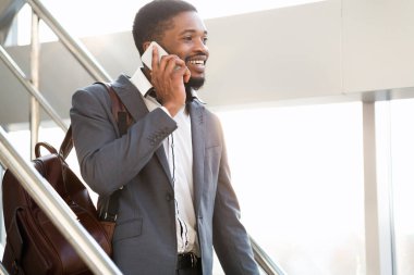 Cep telefonuyla konuşan bir adam havaalanında merdivenlerden iniyor.