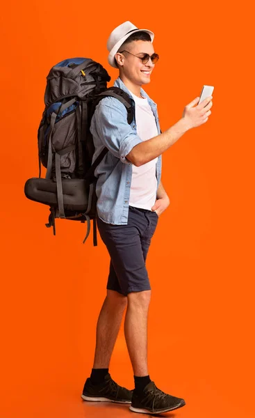 Caminante con aplicación de trekking en el teléfono móvil sobre fondo naranja — Foto de Stock