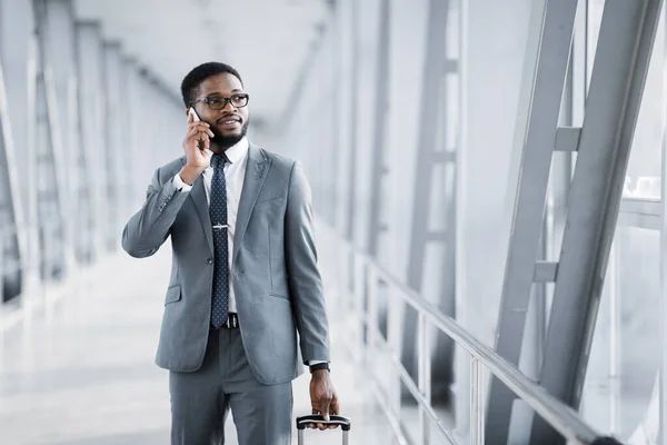 Empresario africano teniendo conversación telefónica caminando con maleta a través del aeropuerto — Foto de Stock