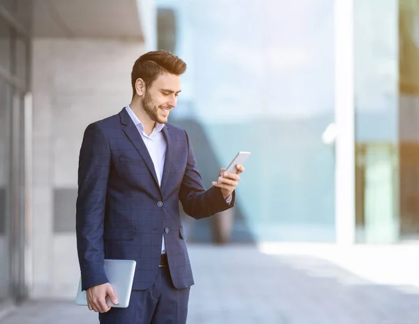 Mosolygós bróker öltönyben, mobiltelefonnal és tablettel a belvárosban, üres hely. — Stock Fotó