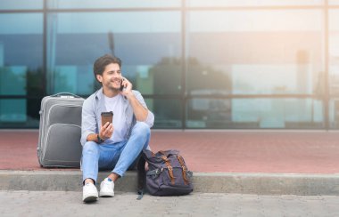 Cep telefonuyla konuşan ve havaalanının dışında kahve içen bir adam.