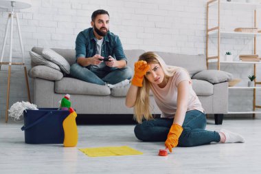 Cleaning and sexism. Man has fun with video games, tired wife clings to her head and do housekeeping clipart