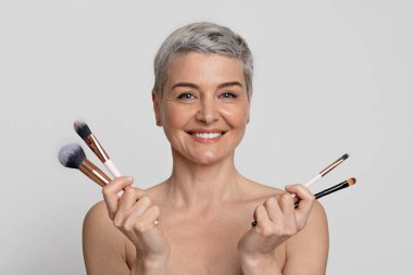 İki elinde makyaj fırçası olan orta yaşlı güzel bir kadının portresi.