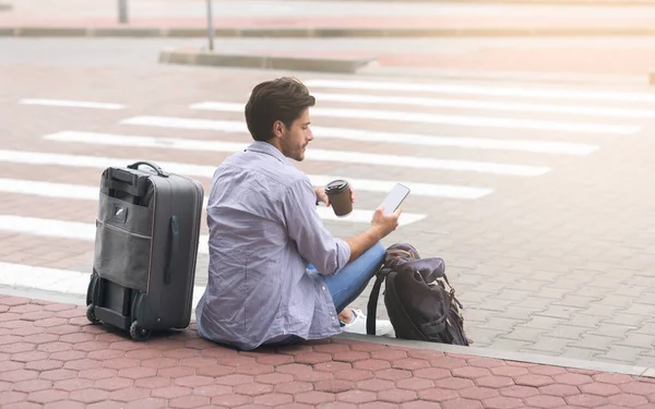 Turista masculino sentado cerca de la terminal del aeropuerto usando smartphone y disfrutando del café — Foto de Stock