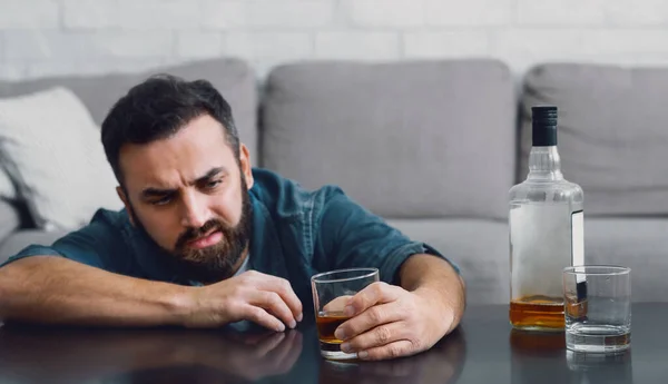 Zničený život alkoholem. Muž sedí u stolu a dívá se na sklo ve své ruce — Stock fotografie