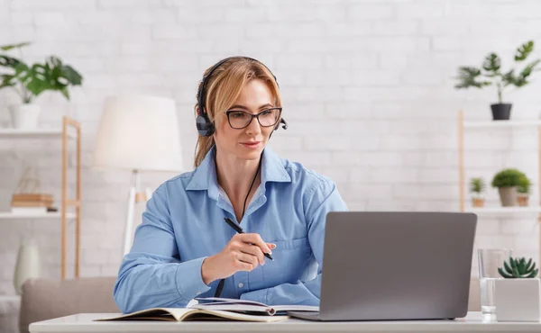 Онлайн консультация психолога. Женщина в очках и наушниках смотрит на ноутбук — стоковое фото