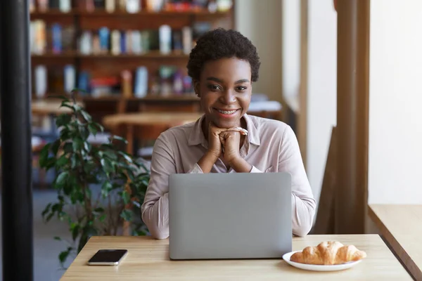 Concepto de aprendizaje electrónico. Atractiva mujer afroamericana utilizando el ordenador portátil para estudiar en línea en la cafetería —  Fotos de Stock
