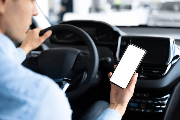 Человек с помощью смартфона сидит в автомобиле в автоцентре — стоковое фото